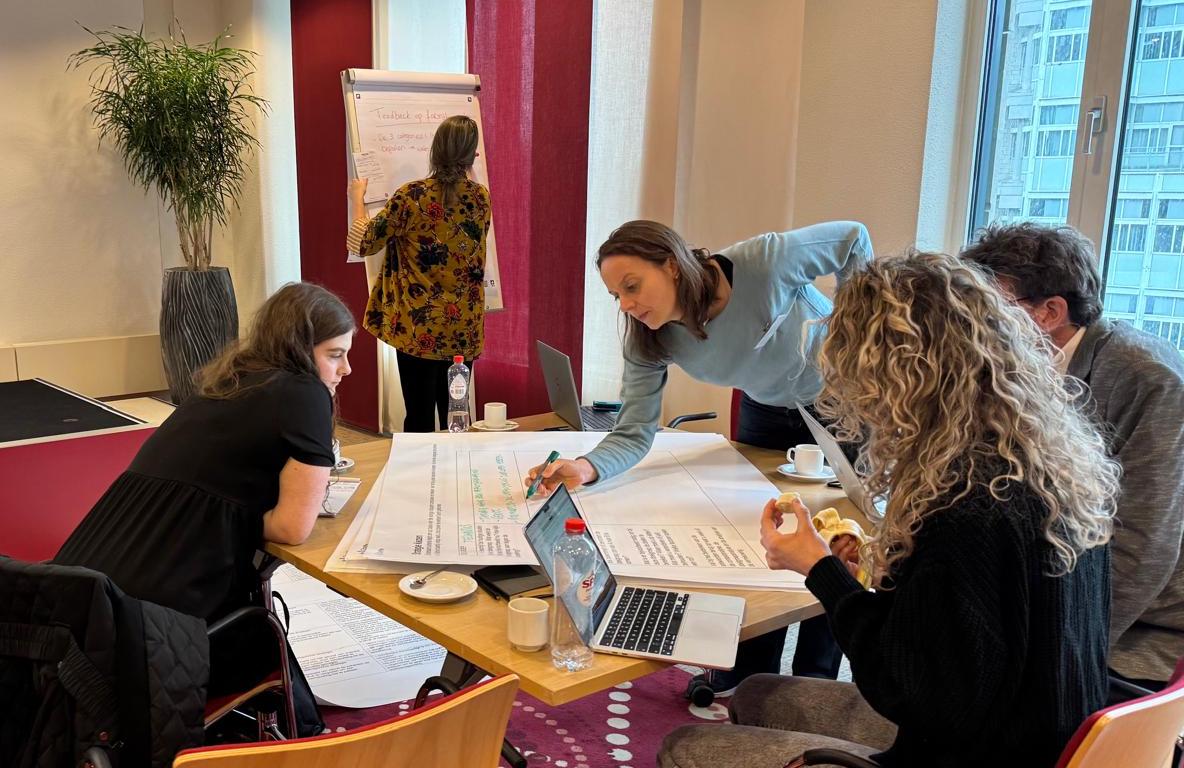 Foto van groep discussiërende mensen rond tafel met documenten